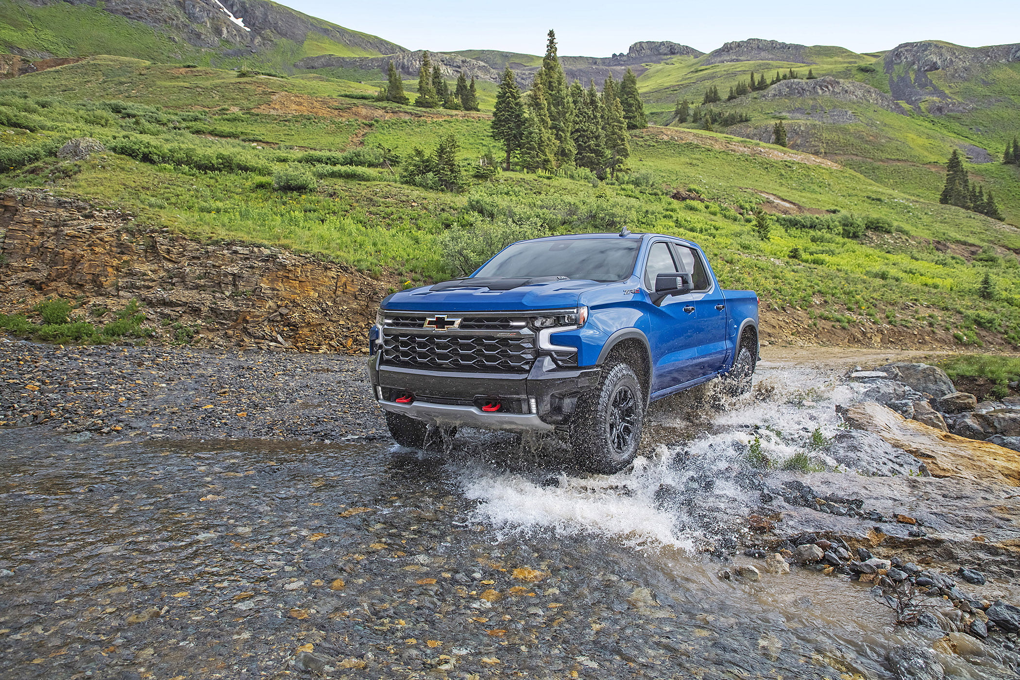A blue 2022 Chevrolet Silverado off-roading through a mountain stream.