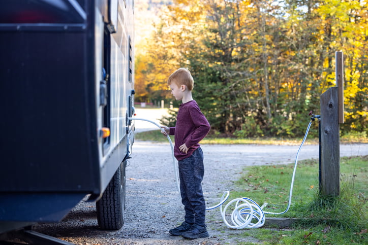 A 10-year-old boy with red hair is filling the freshwater tank in his family’s RV.