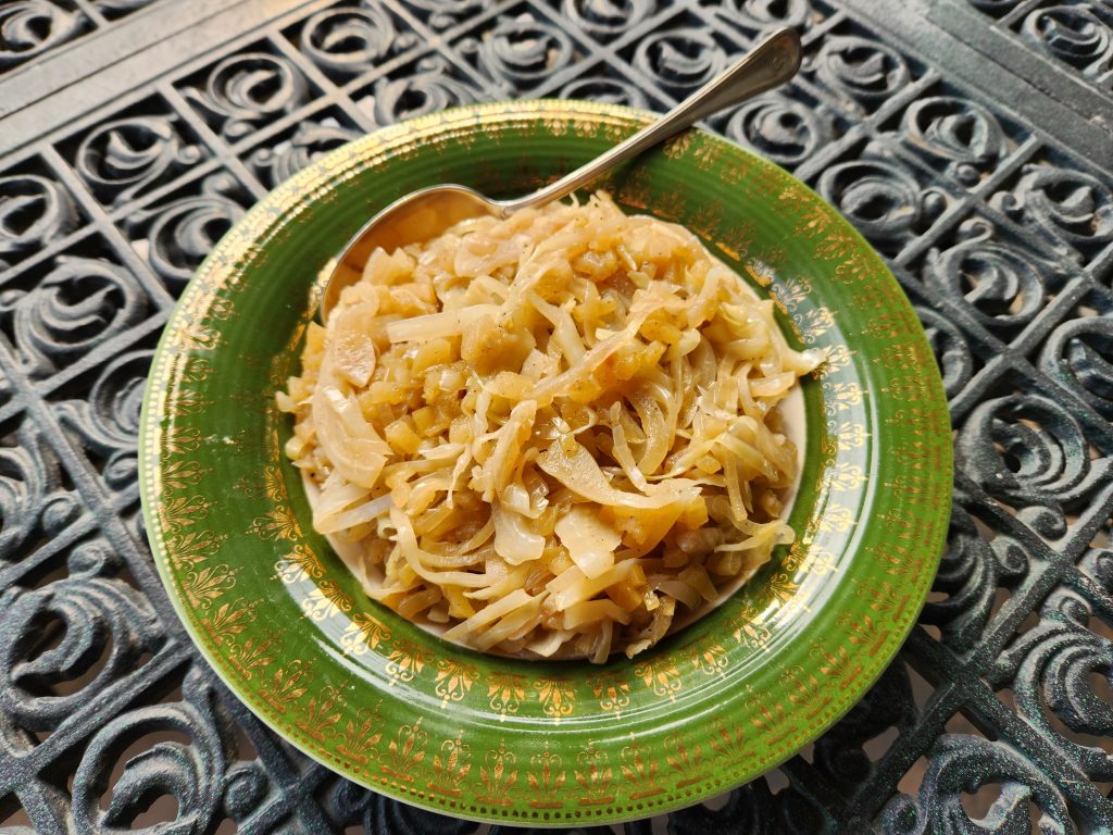 A green bowl with decorative gold details, full of sweet cabbage apple salad.