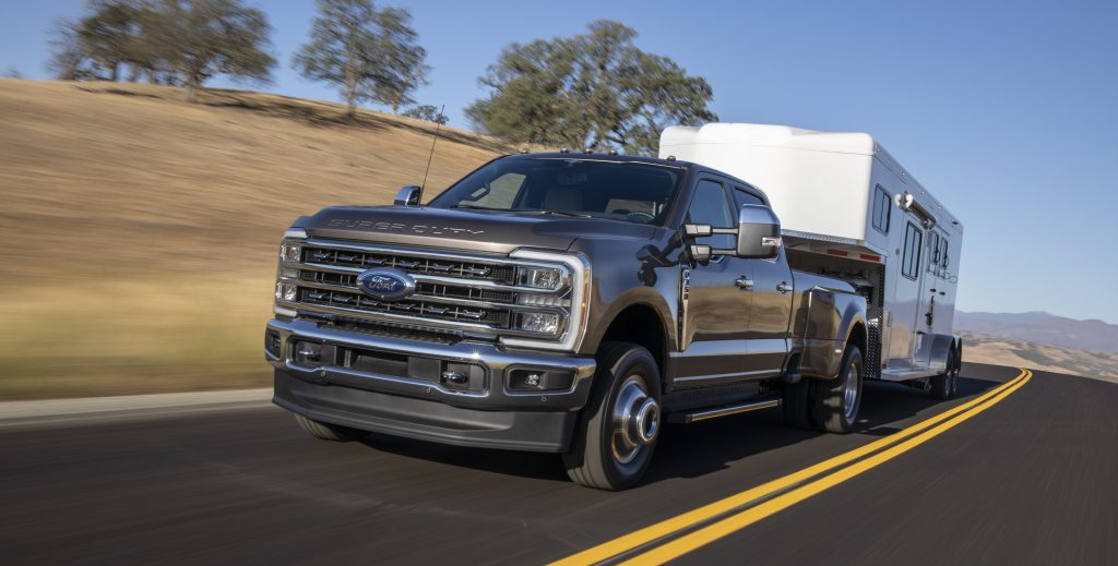 A Ford F-Series Super Duty pickup truck driving on a highway, towing a fifth-wheel trailer.