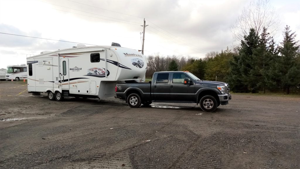 A grey pickup truck towing a fifth-wheel trailer is parked.