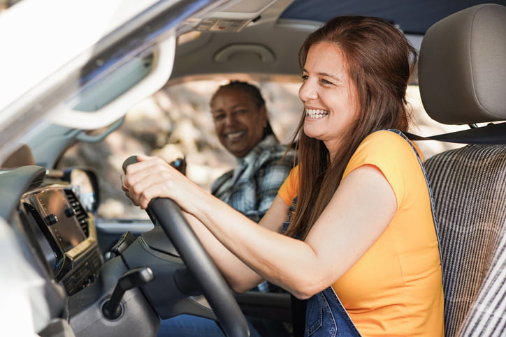 A woman is in the driver seat of an RV with her partner in the passenger seat; they’re laughing as they head out on their first trip.