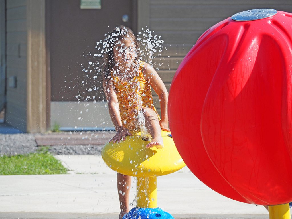 A child in a swimsuit playing at a splash pad on a hot summer day.