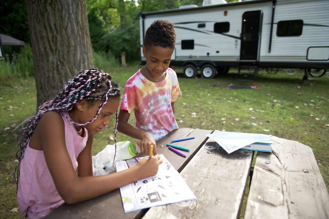 Two kids colouring outside at a picnic table at an RV park. Keyword: RVing with kids