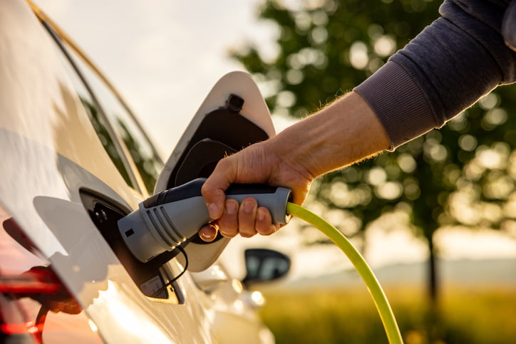 A close-up of someone connecting a charging station hook-up to their electric vehicle’s charging port.