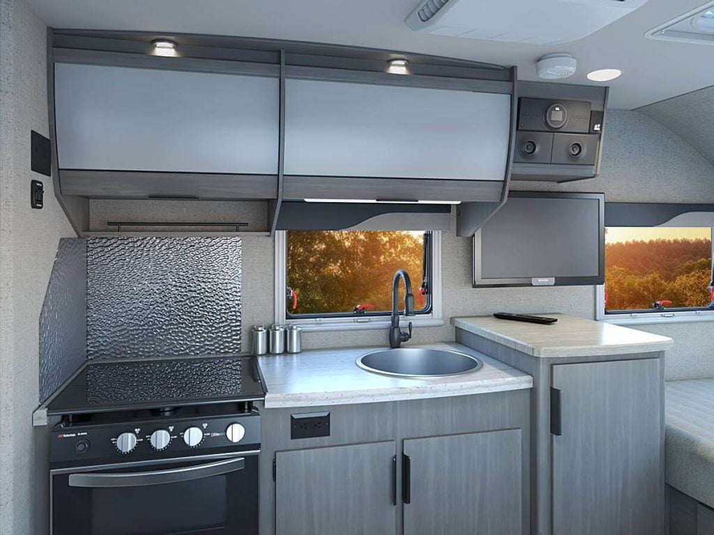 Lance 1475 RV Trailer kitchen picturing two upper storage spaces, three lower cabinets, sink, stove, and oven.