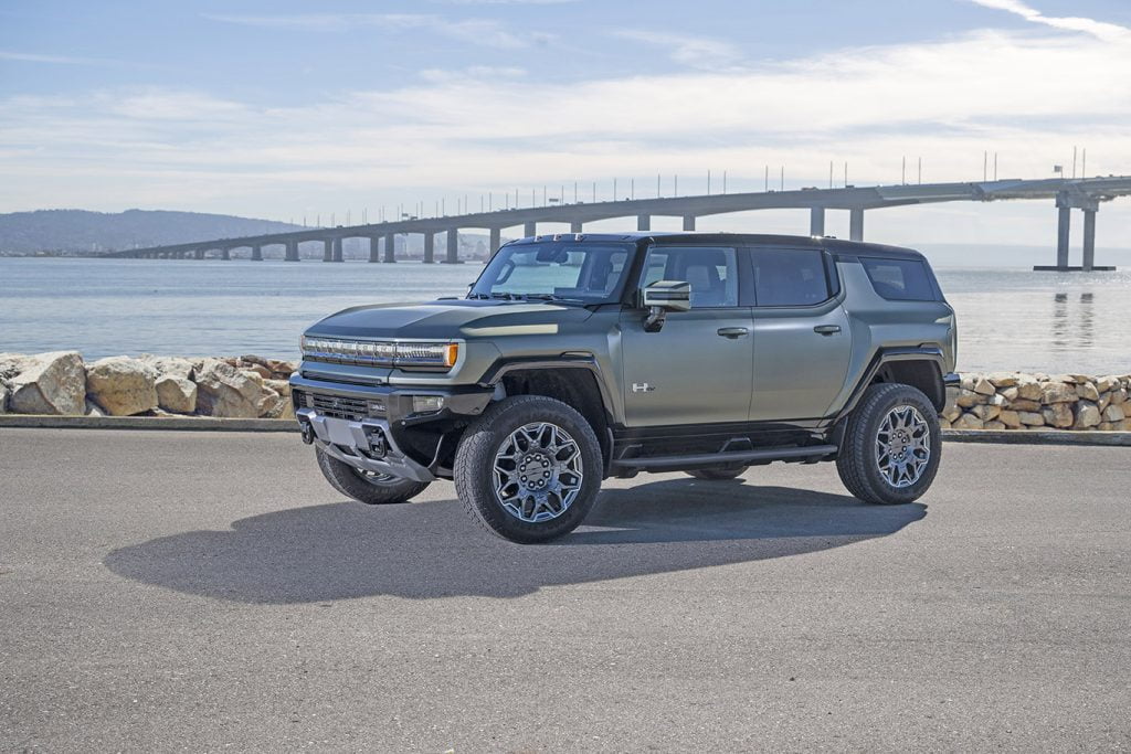 2024 GMC HUMMER EV SUV in Moonshot Green Matte parked near water and a bridge.