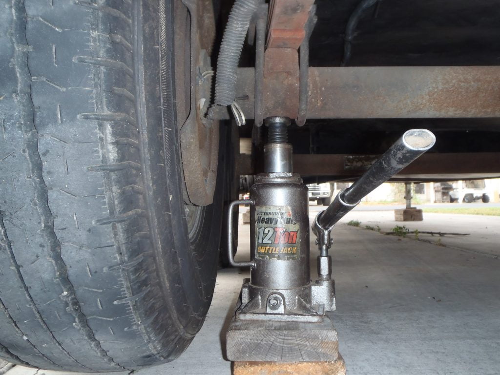 A close-up of a 12 tonne bottle jack on top of two stacked 2x4 wooden blocks under a trailer.