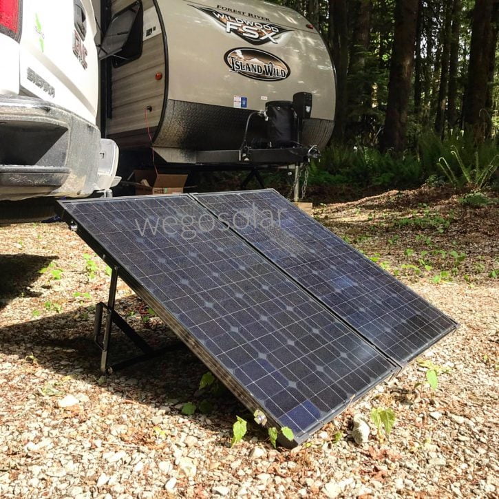 An image of a solar panel folding kit placed in front of a trailer and a truck in a wooded area. The folding kit consists of portable solar panels neatly arranged and connected, ready to harness solar energy. The trailer and truck create a picturesque scene amidst the trees, highlighting the versatility and convenience of the solar panel kit for off-grid adventures.