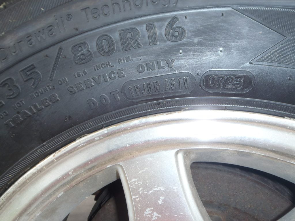 A close-up of a trailer tire, demonstrating how to find the DOT code that indicates the week and year of manufacture.