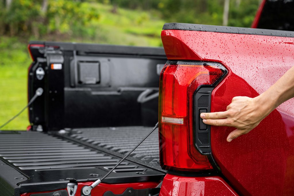 Rear view of a red Toyota Tacoma with a man's hand pointing at the lights, highlighting the vehicle's distinctive taillights and adding a human element to the composition.