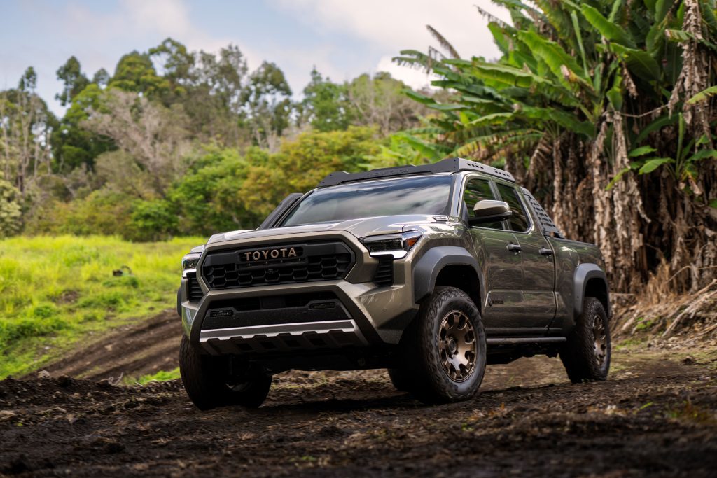 A 2024 silver-coloured Toyota Tacoma Trail Hunter navigating the rugged roads of Hawaii, with lush greenery in the background, showcasing the vehicle's adventurous spirit amidst the beautiful natural landscape.