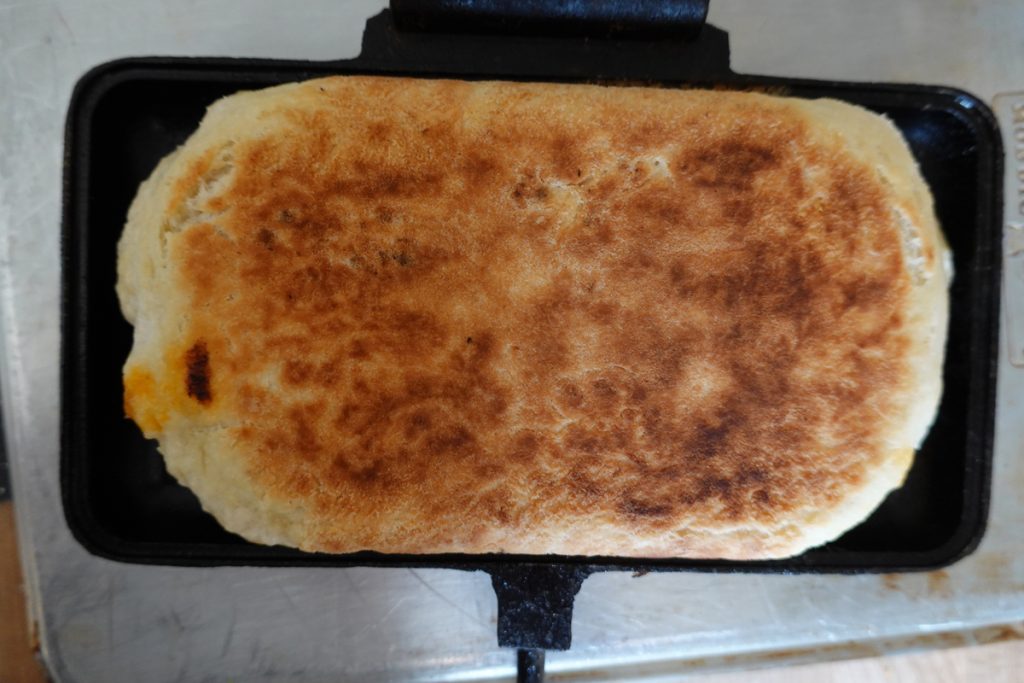 An image of golden-brown, crispy food cooked in a pie iron. The delicious meal is perfectly cooked and has a tantalizing appearance. The pie iron has created a crispy exterior.