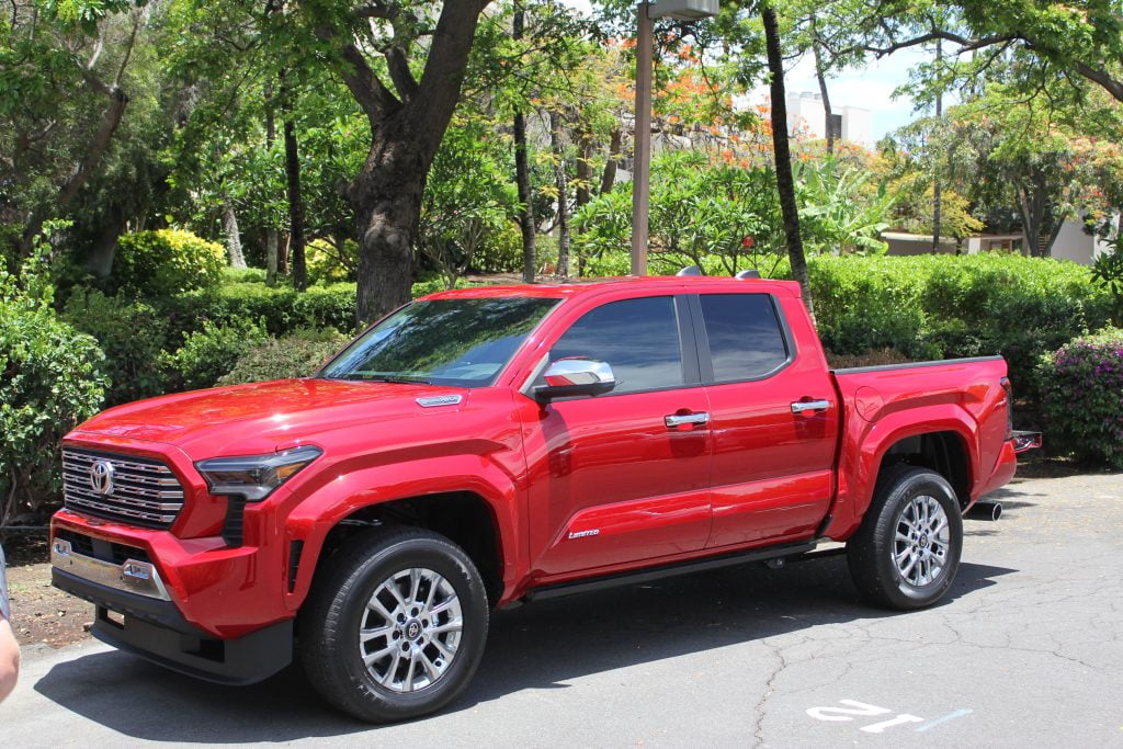 A vibrant red Toyota Tacoma four-door truck parked amidst the lush greenery of the Hawaiian landscape.