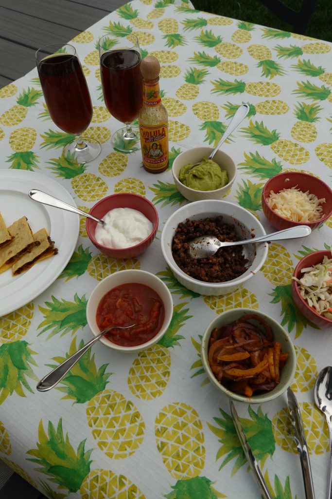 assortment of taco toppings spread on a table with a charming pineapple-patterned tablecloth. The toppings include fresh vegetables, zesty sauces, shredded cheese, and other delectable ingredients, inviting a delightful and flavorful taco feast.