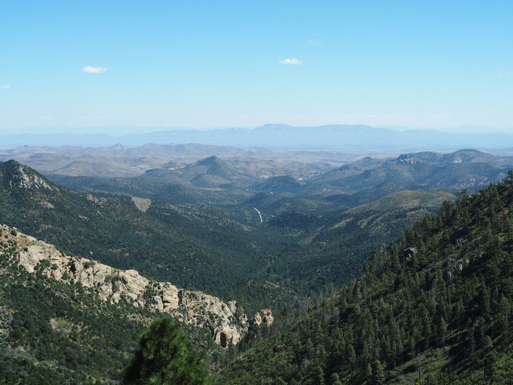 A view of a valley with trees and mountains. Framed with a blue open sky.