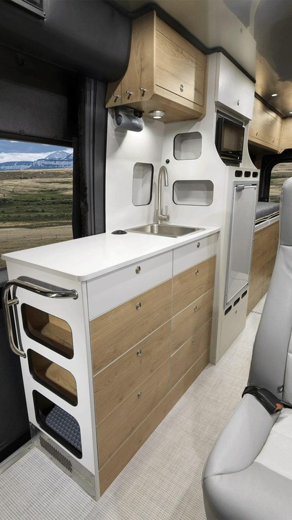 2024 Airstream Rangeline interior with many cabinets, attached to one of the cabinets is a wireless speaker and light mounted to an overhead counter. There is also a fridge