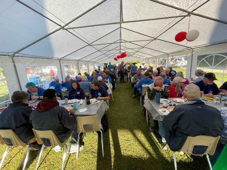An image of a large outdoor tent with windows and lots of bright light. There are rows of tables with people enjoying great food and excellent company.