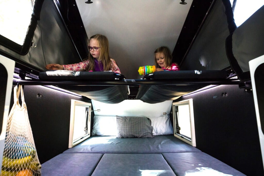The sleeping area of this RV shows plenty of room! In the upper sleep area, there are two children reading. Both are enjoying the quiet time while RVing.