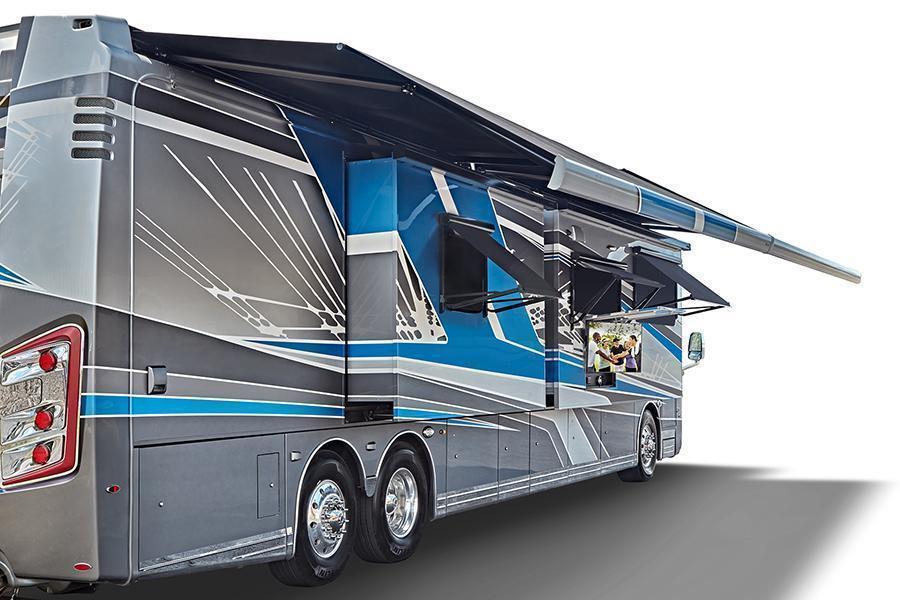 An image of a coach motorhome. The RV is a stunning grey with with and blue trim. The awning is open.