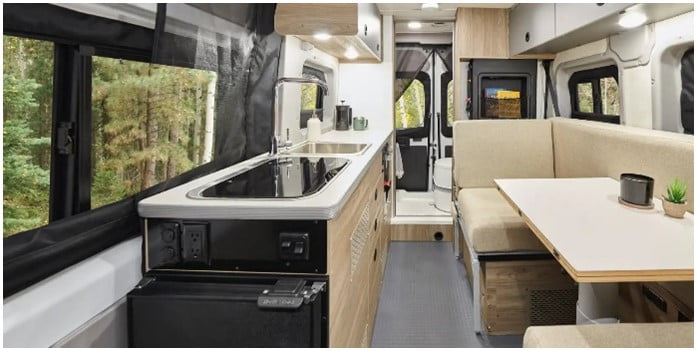 The interior of the Winnebago has a large sink with a beautiful wide window behind the sink for a great view while doing dishes! There is a table with seating for two across from the sink