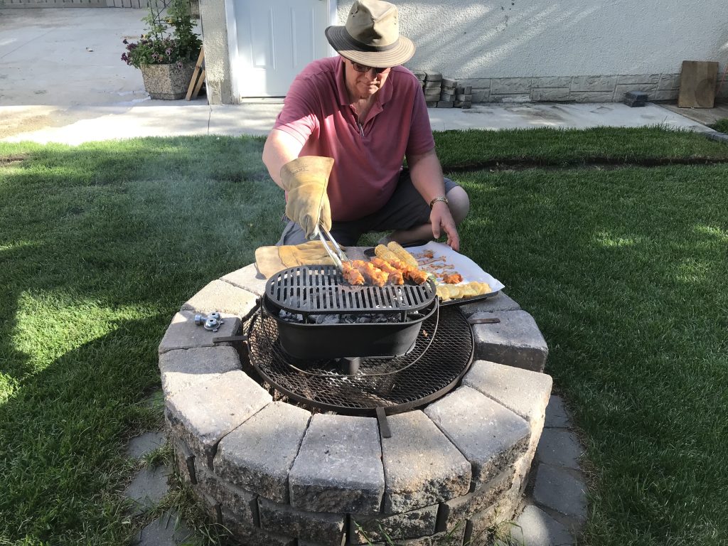 A man adding food to a grill in his backyard with a pair of tongs.