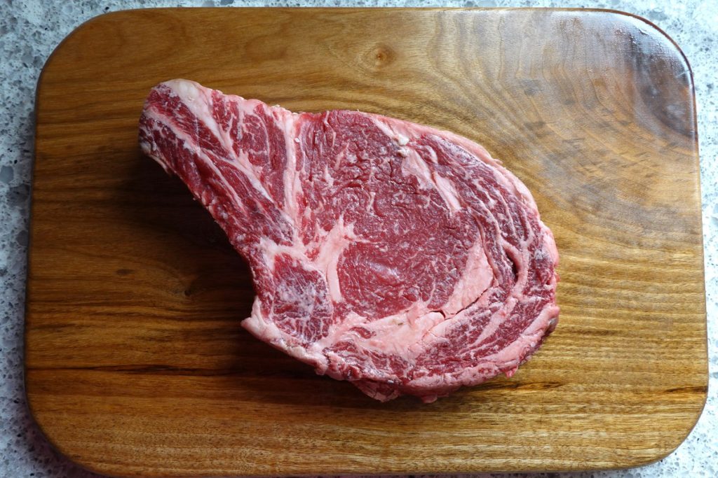 A Bone-in Rib Steak on a cutting board before it’s seasoned.