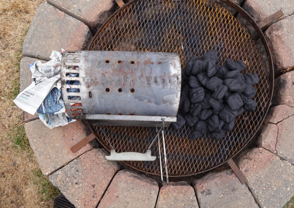 Chimney starter with briquettes next to it on a grill.