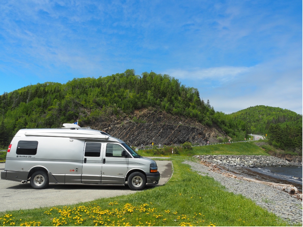 A silver Roadtrek 210 motorhome is parked next to the shore in Gaspé, Quebec.