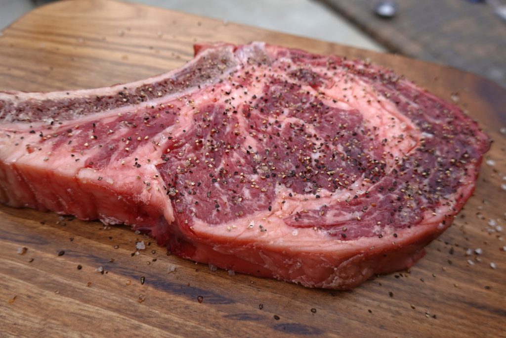 A seasoned Bone-in Rib Steak on a cutting board.