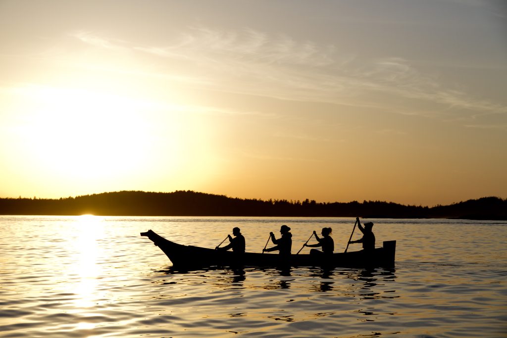 4 people paddling in a canoe with the Sun setting in the back on Meares Island