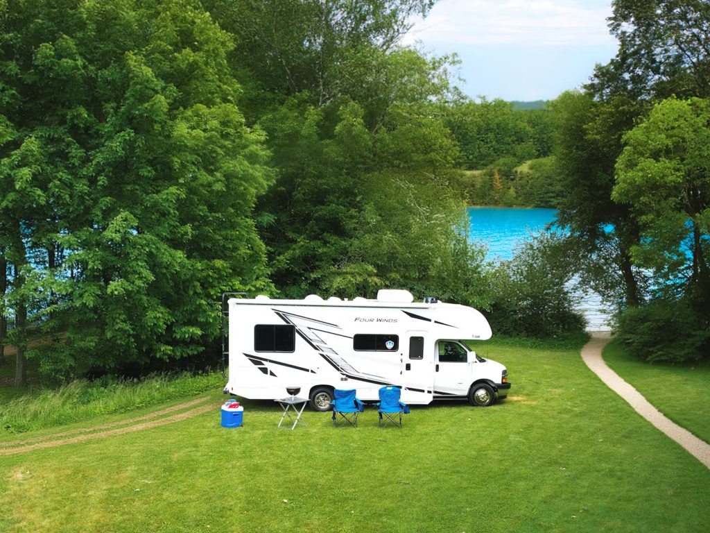 Thor Motor Coach Class C parked in a forest area by a lake.