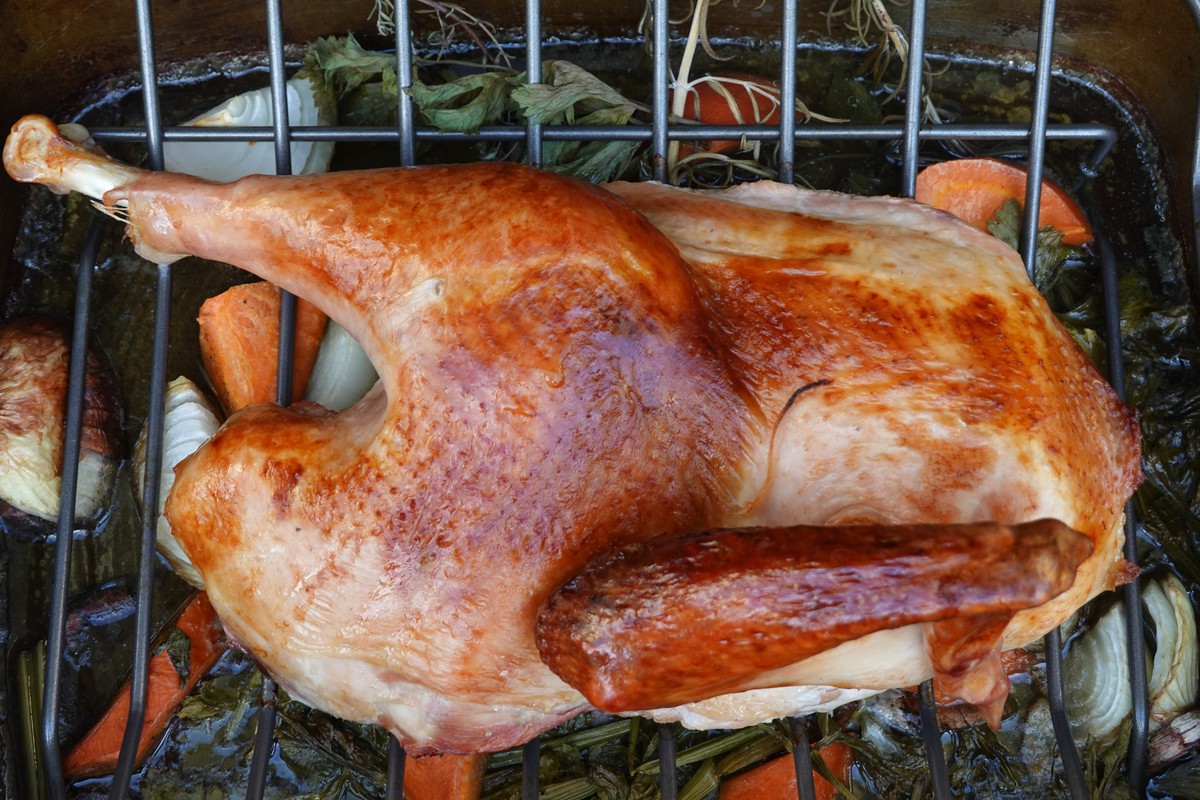 Cooked Turkey laying on a rack over cooked vegetables in a pan.