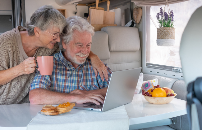 A happy couple looking at their laptop in their Motorhome with smiles on their faces.