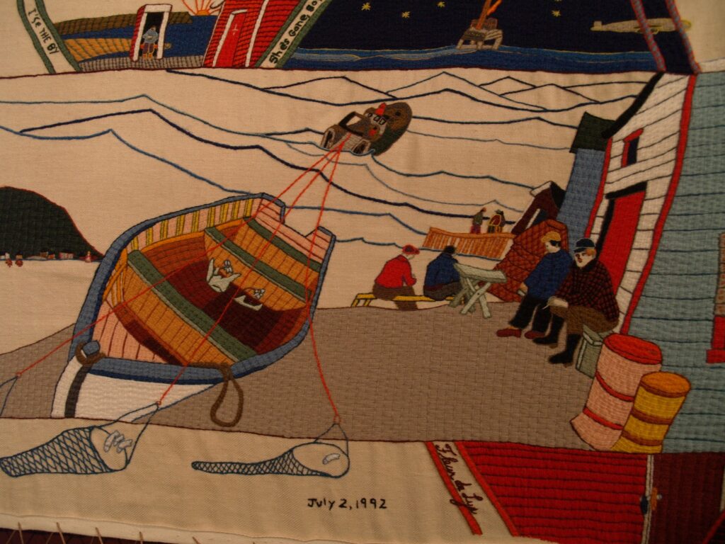 An embroidered scene depicting a fishing village with boats, fishermen, and buildings.