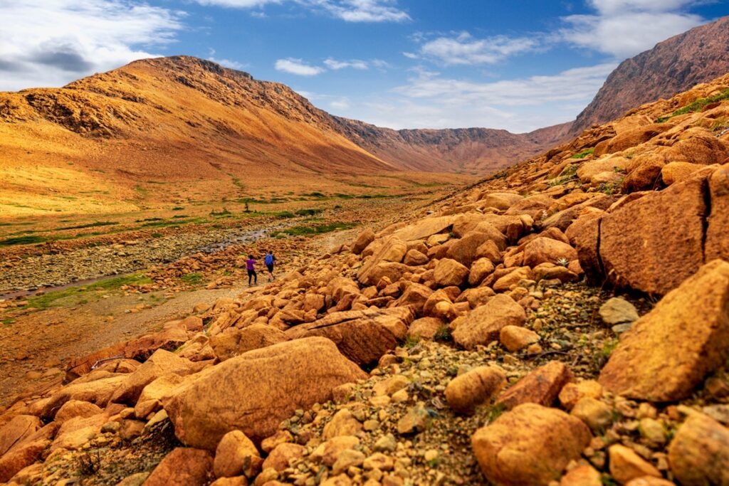 Two hikers in a rocky mountain landscape under a partly cloudy sky.