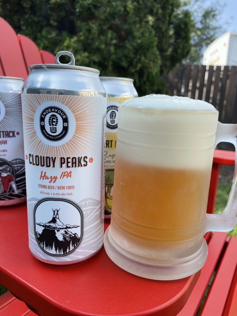 An opened beer sits next to a mug of beer on an outdoor chair’s armrest.