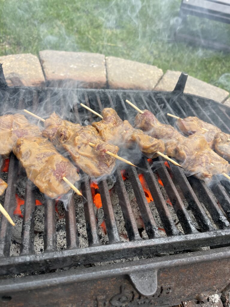 Skewered meat being grilled on a charcoal BBQ.