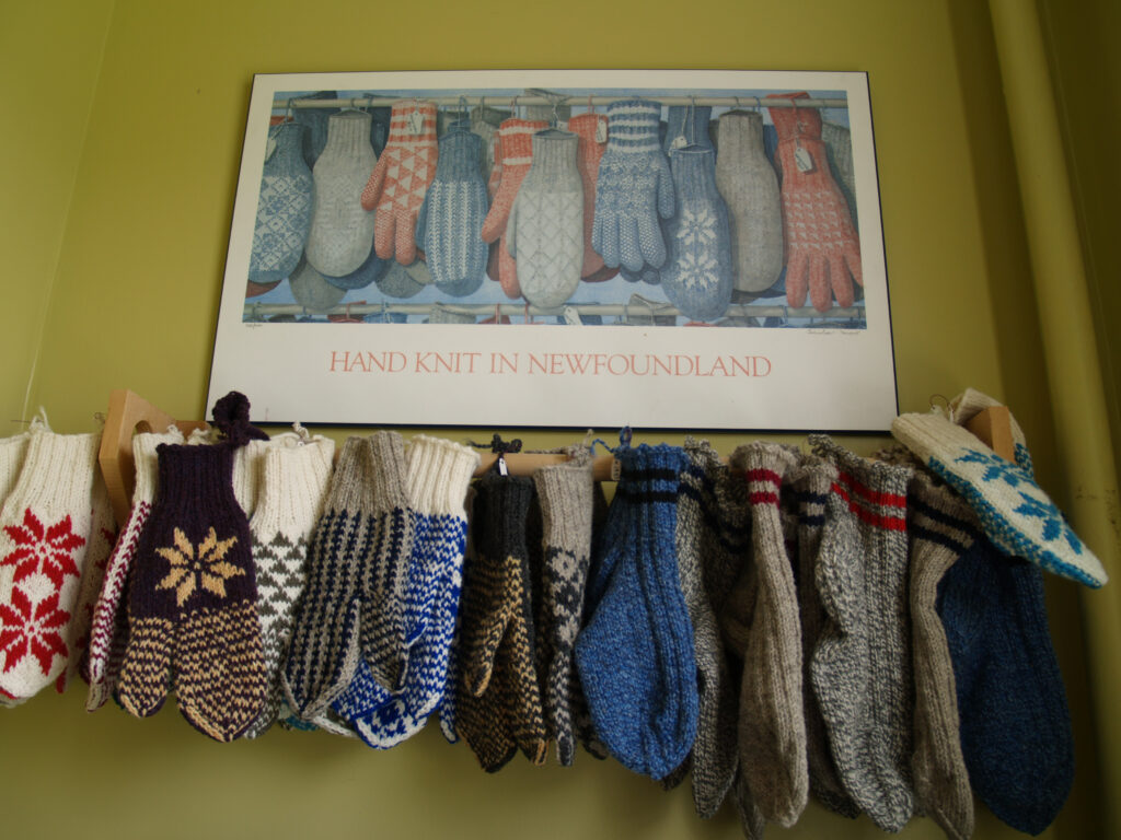 A collection of colourful hand-knit mittens hanging on a line beneath a framed picture labelled