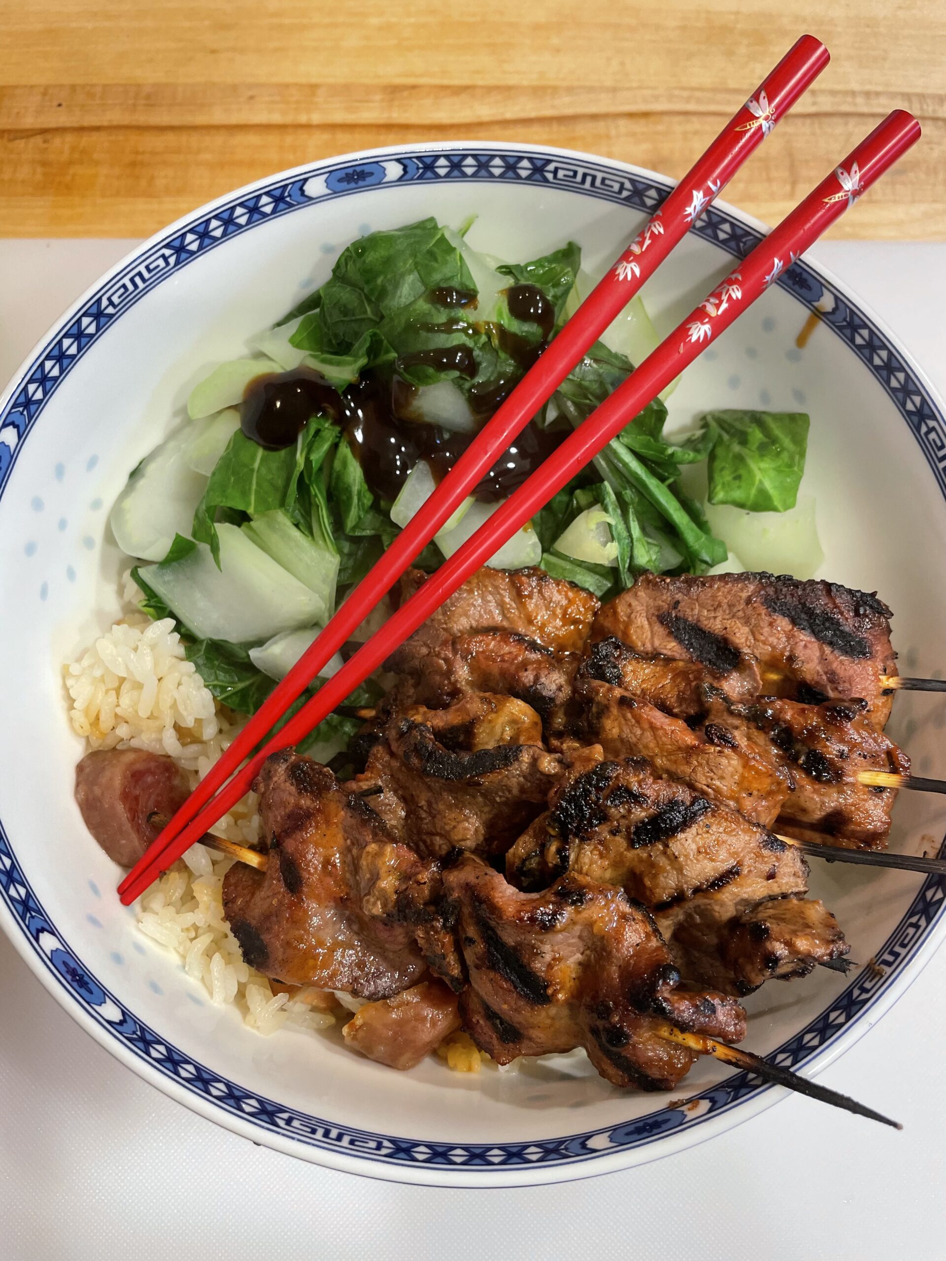 A plate of sticky rice, steamed bok choy, and peanut-free satay beef skewers.