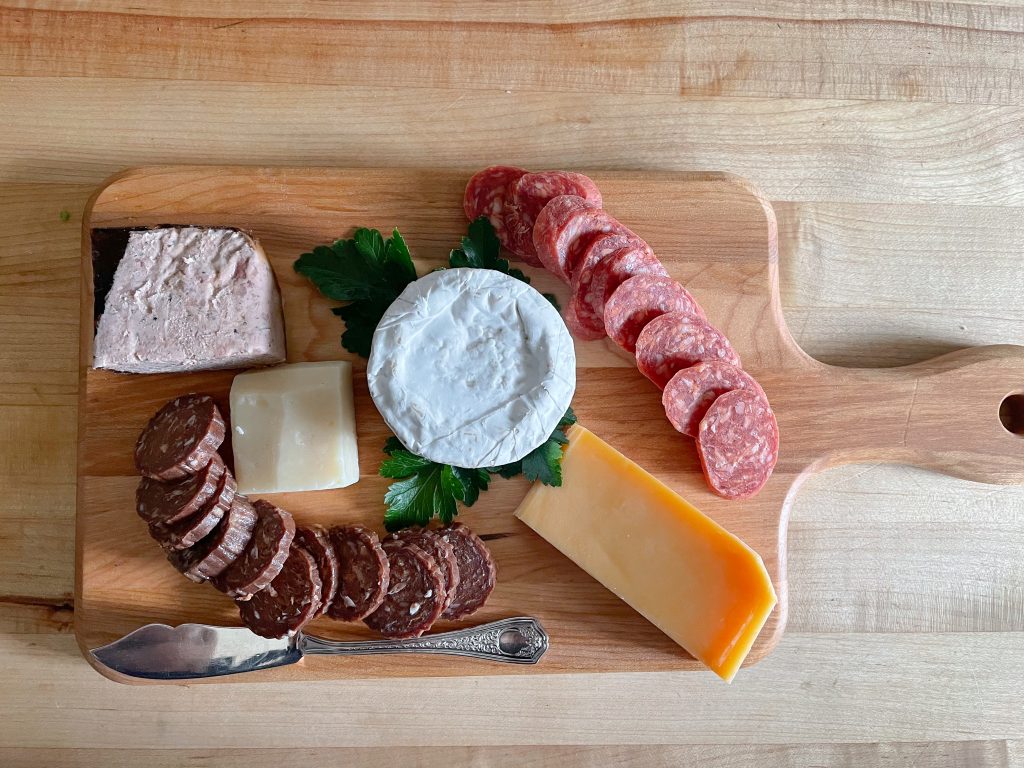 Charcuterie board with pepper pate, brie, sliced spicy cacciatore, aged Gouda, mild summer sausage, and Emmenthal.