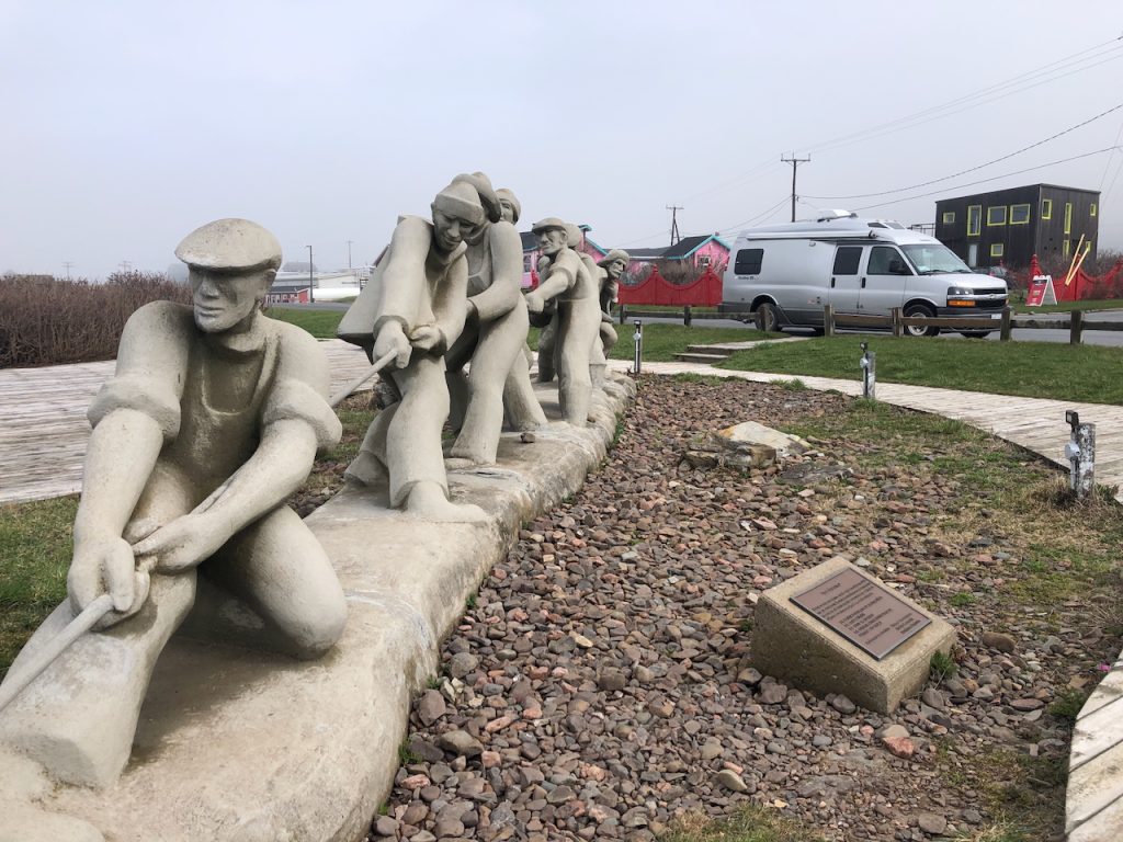 A row of life-sized stone statues depicts fishers pulling together on a rope, commemorating the importance of the fishery on Îles de la Madeleine.