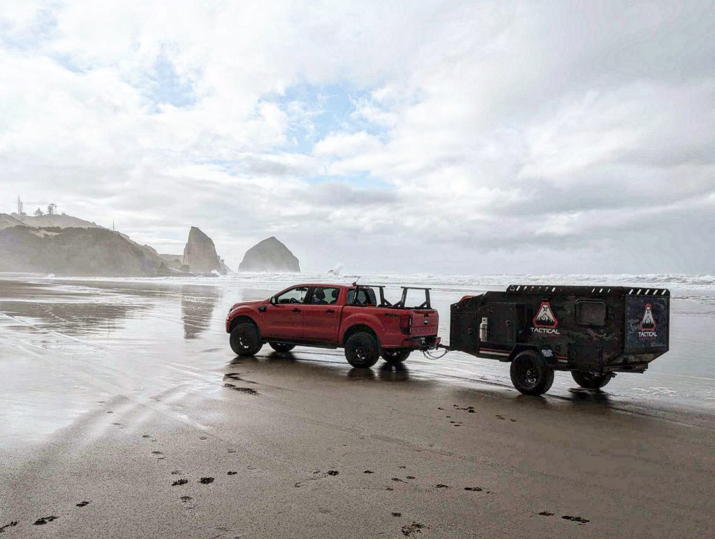 A red truck is seen pulling a Tactical Overland Trailer on a beach.