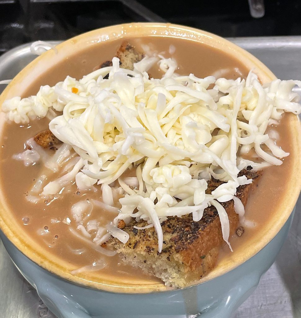 Image of shredded cheese on top of a bowl of French onion soup.