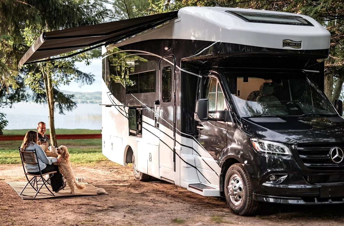 A coupe is seen sitting outside under the awning of their Newmar Freedom Aire motorhome with their dog.