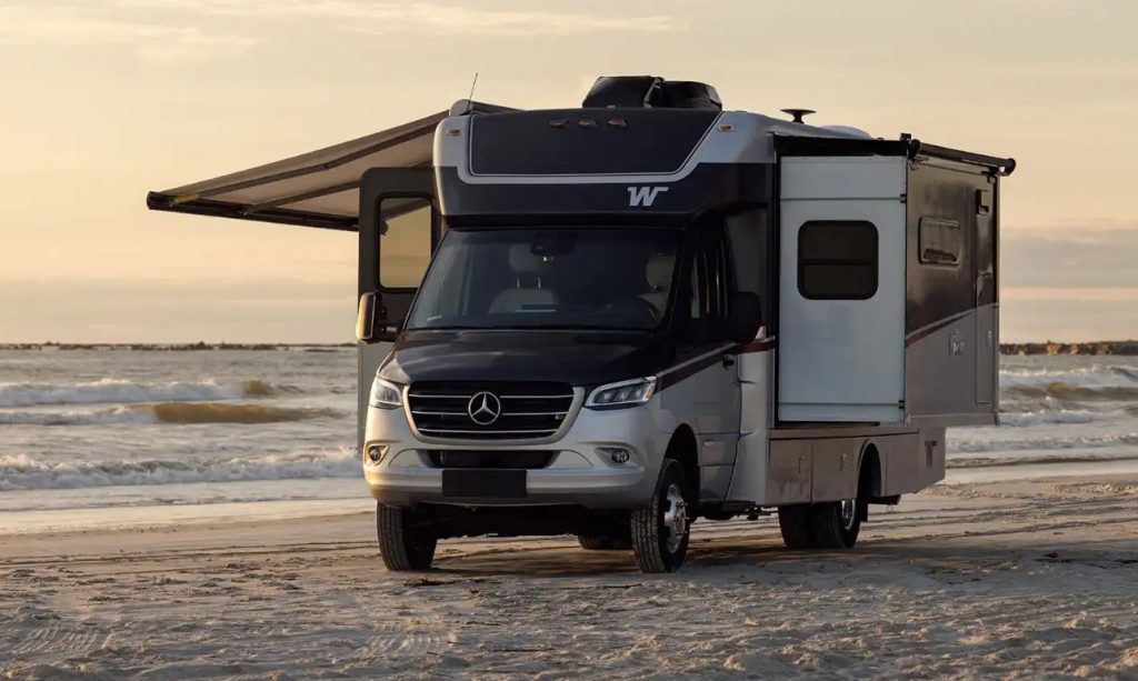 he 2026 Winnebago View Class C motorhome is seen parked at the beach during a sunset with the awning extended.