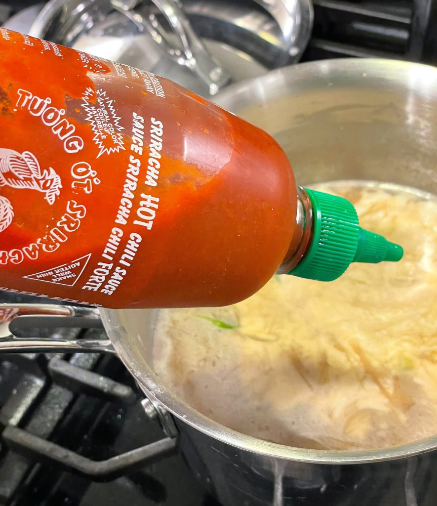 Image showing sriracha hot sauce being added to pot of soup.