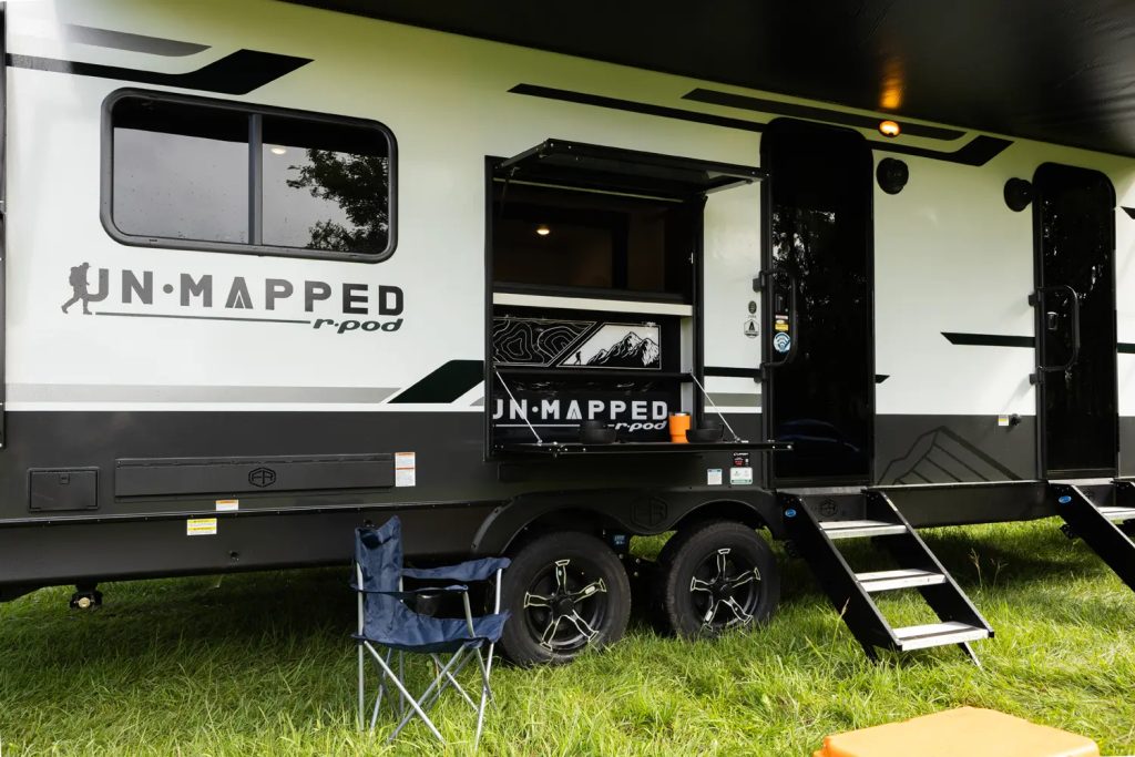 The 2026 Forest River Un-Mapped 24RK parked on a grass campsite with the steps out and a folding chair next to it.