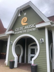 The entrance of the Celtic Music Interpretive Centre featuring a green exterior, a large circular archway, and signage with a spiral logo under an overcast sky.