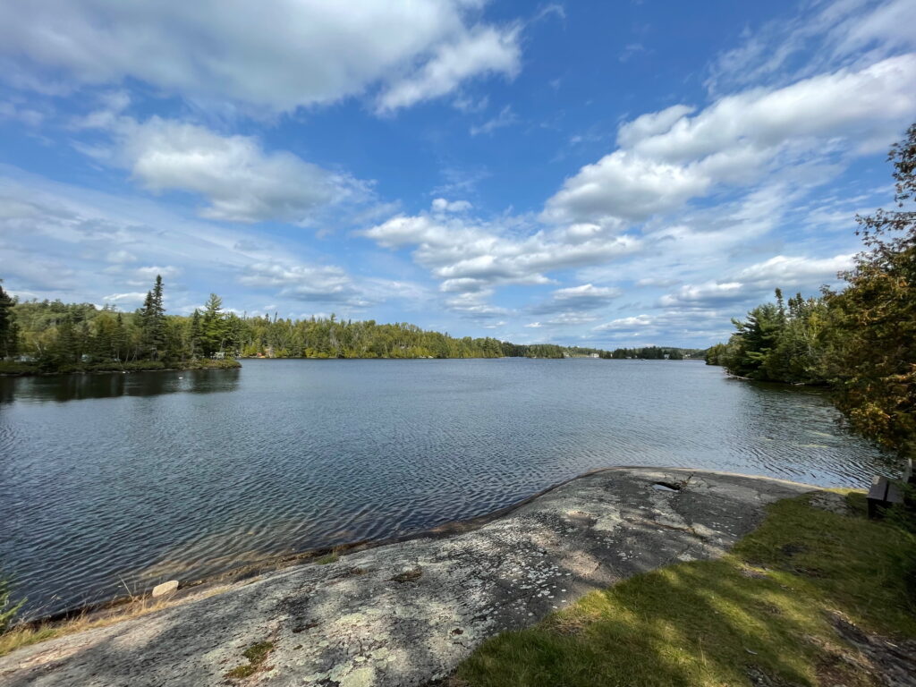 A lake with a rocky shoreline surrounded by trees on a sunny day.
